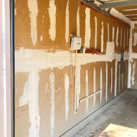 A garage wall mid-repair by JC Painting Services, with joint compound worked over the drywall seams and screw lines ready for sanding