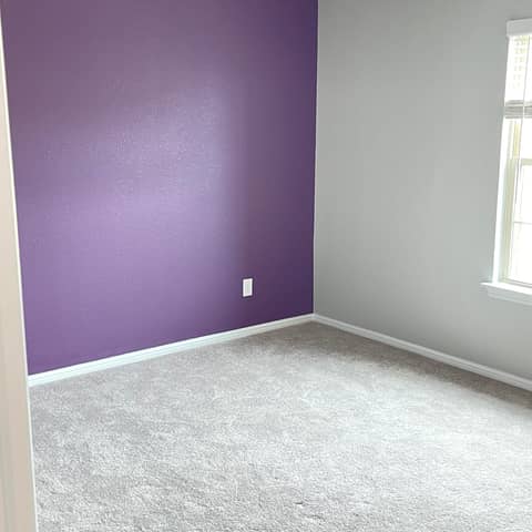 A finished bedroom painted by JC Painting Services, with a deep purple accent wall meeting soft grey walls and white baseboards